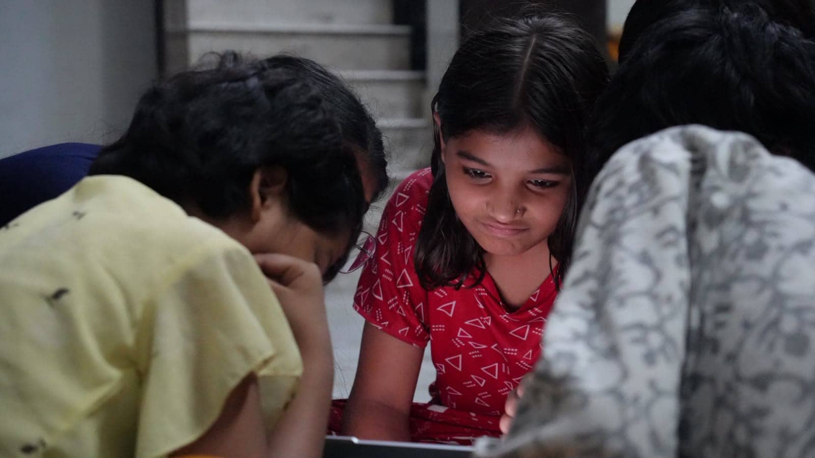 A girl in a red top concentrates on a laptop screen.