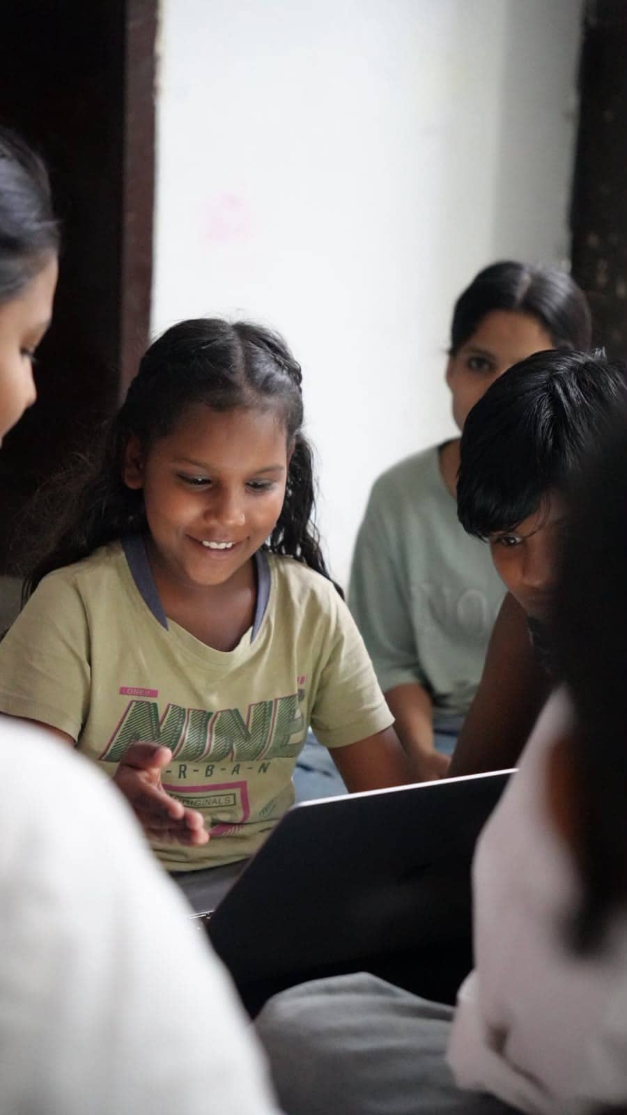 A girl smiles while working at a laptop beside a volunteer.